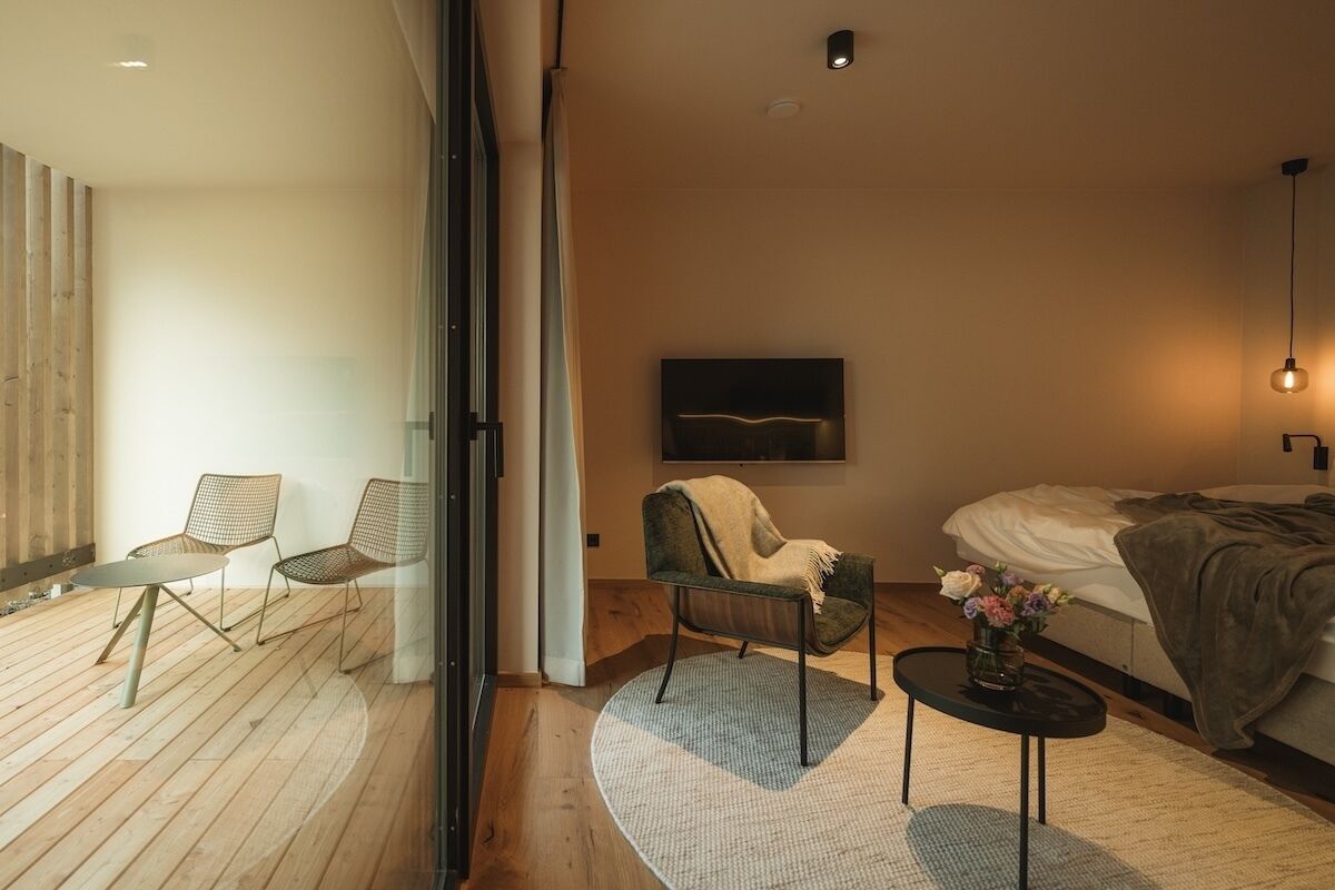 Un dormitorio moderno con cama, televisor en la pared y una zona de estar con sillas y una mesita.