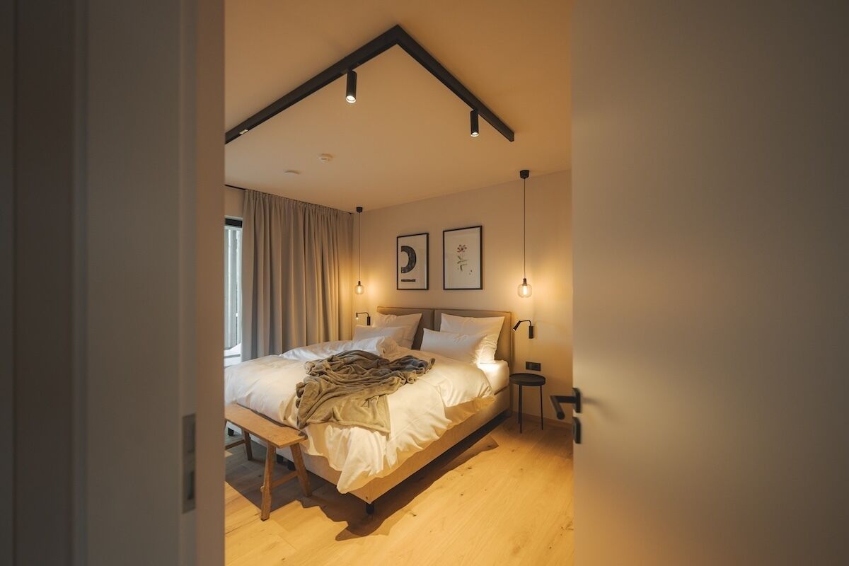 A bedroom with a bed, bedside tables, and wall-mounted lights.