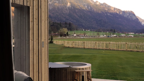 Eine Holzterrasse mit Whirlpool, Sitzgelegenheit und Bergblick.