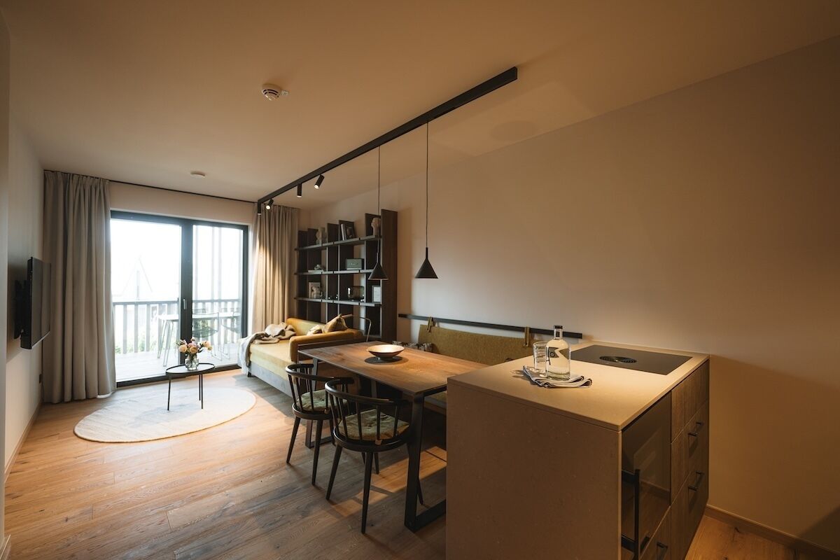 A modern living room with a dining area, a kitchen, and a balcony with a view.