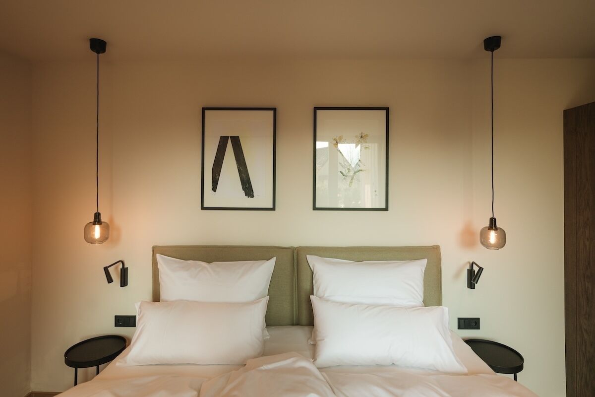 A double bed with white linens, two wall-mounted picture frames, and two black nightstands with lamps.