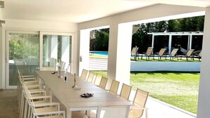 Un comedor moderno con una mesa larga y sillas, ventanas amplias y vistas a una piscina y jardín.