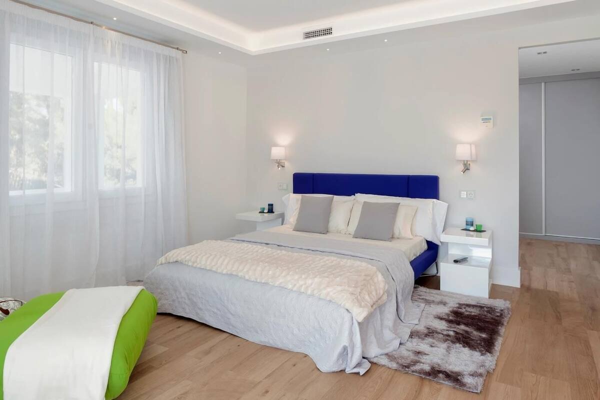 Une chambre d’hôtel moderne, dotée d’un grand lit, de tables de chevet et offrant une vue sur l’extérieur à travers de fines rideaux.