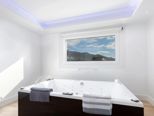 Un baño moderno con una bañera grande, una ventana con vistas a la ciudad y un tragaluz.
