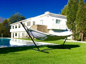 A modern white house with a stone facade, a swimming pool, and a hammock on the lawn. - Top Luxury Marbella Villa  (Marbella)