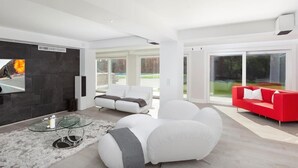 Una sala moderna con chimenea, sofás blancos, un sofá rojo y una mesa de centro de vidrio.