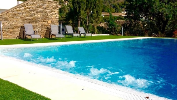 Una piscina con agua azul cristalina, rodeada por un muro de piedra y una zona verde.