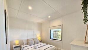 Ein Schlafzimmer mit Bett, Nachttischlampen, einem Fenster und einer Pflanze.