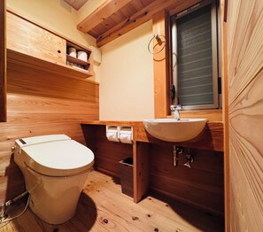 A wooden bathroom with a toilet, sink, and window.
