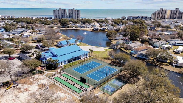A residential area with a tennis court, a body of water, and high-rise buildings in the background. - Beautiful 4B 3.5BA in Oceanside Village - Pet friendly! 2 Golf carts included! (Surfside Beach)