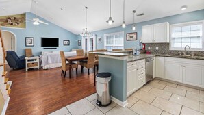 A kitchen with white cabinets, a dining area with a table and chairs, and a trash can. - Beautiful 4B 3.5BA in Oceanside Village - Pet friendly! 2 Golf carts included! (Surfside Beach)