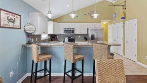 A kitchen with white cabinets, a microwave, a refrigerator, and a bar area with wicker chairs. - Beautiful 4B 3.5BA in Oceanside Village - Pet friendly! 2 Golf carts included! (Surfside Beach)