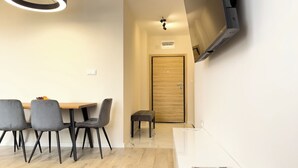 Un comedor moderno con una mesa de madera y cuatro sillas grises, un pequeño banco y un televisor de pantalla plana montado en la pared.