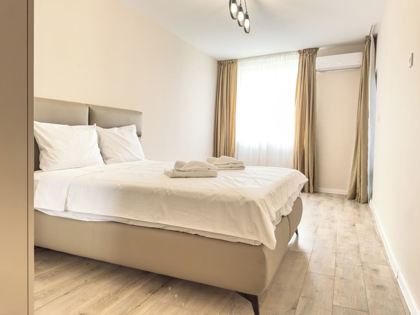 A neatly made bed with white linens and a folded towel, a headboard, and a wooden floor.