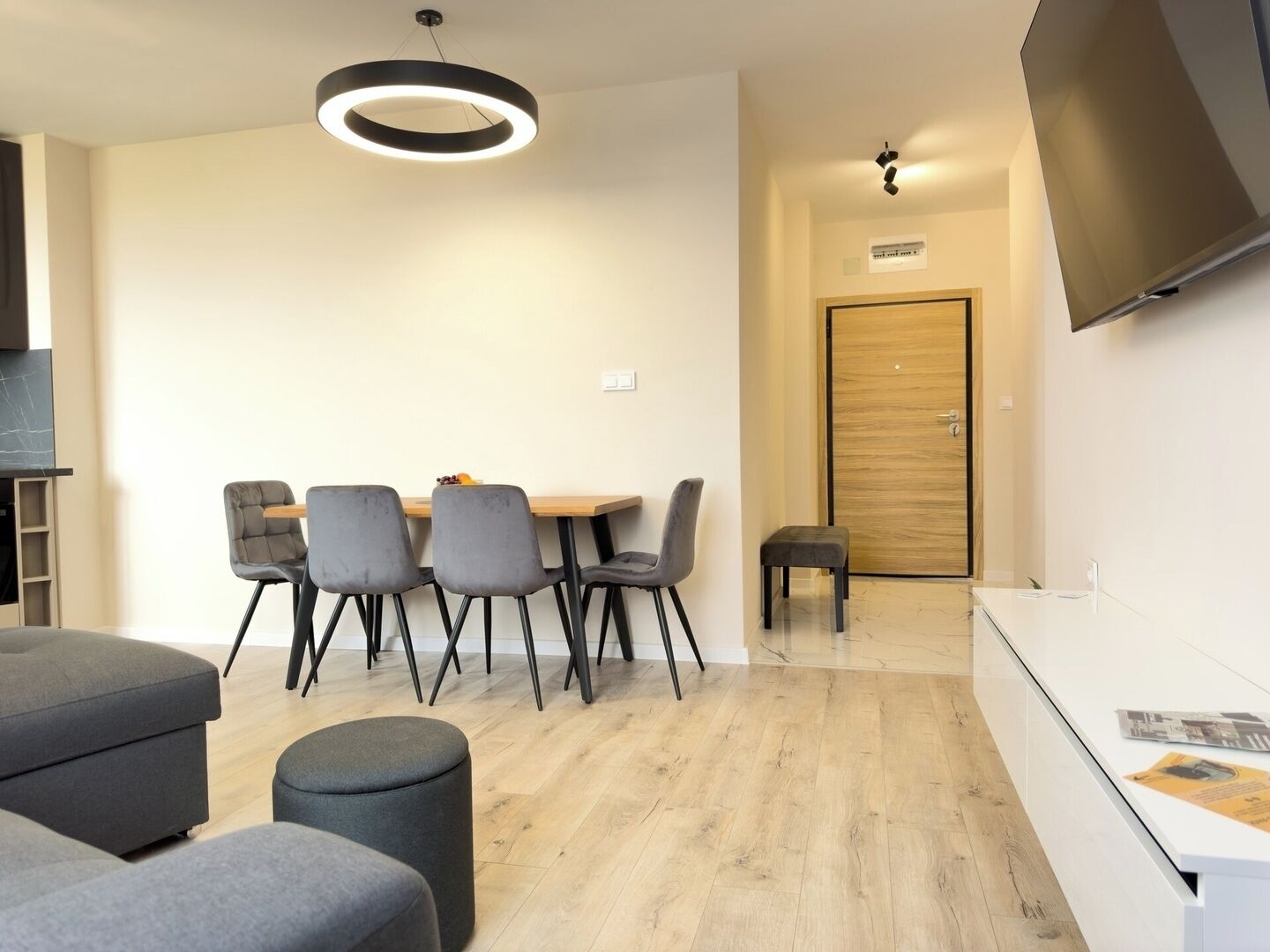Een moderne woonkamer met een ronde tafel, grijze stoelen, een grijze bank en een klein pouf.