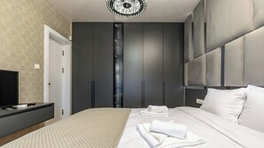 Een moderne slaapkamer met een groot bed, een televisie op een dressoir en een kledingkast met spiegel.