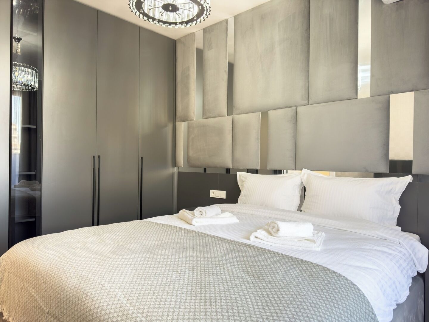 A modern bedroom with a large bed, grey wardrobe, and a chandelier.