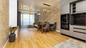 Een moderne keuken met een eethoek, houten vloeren en een groot raam met gordijnen.
