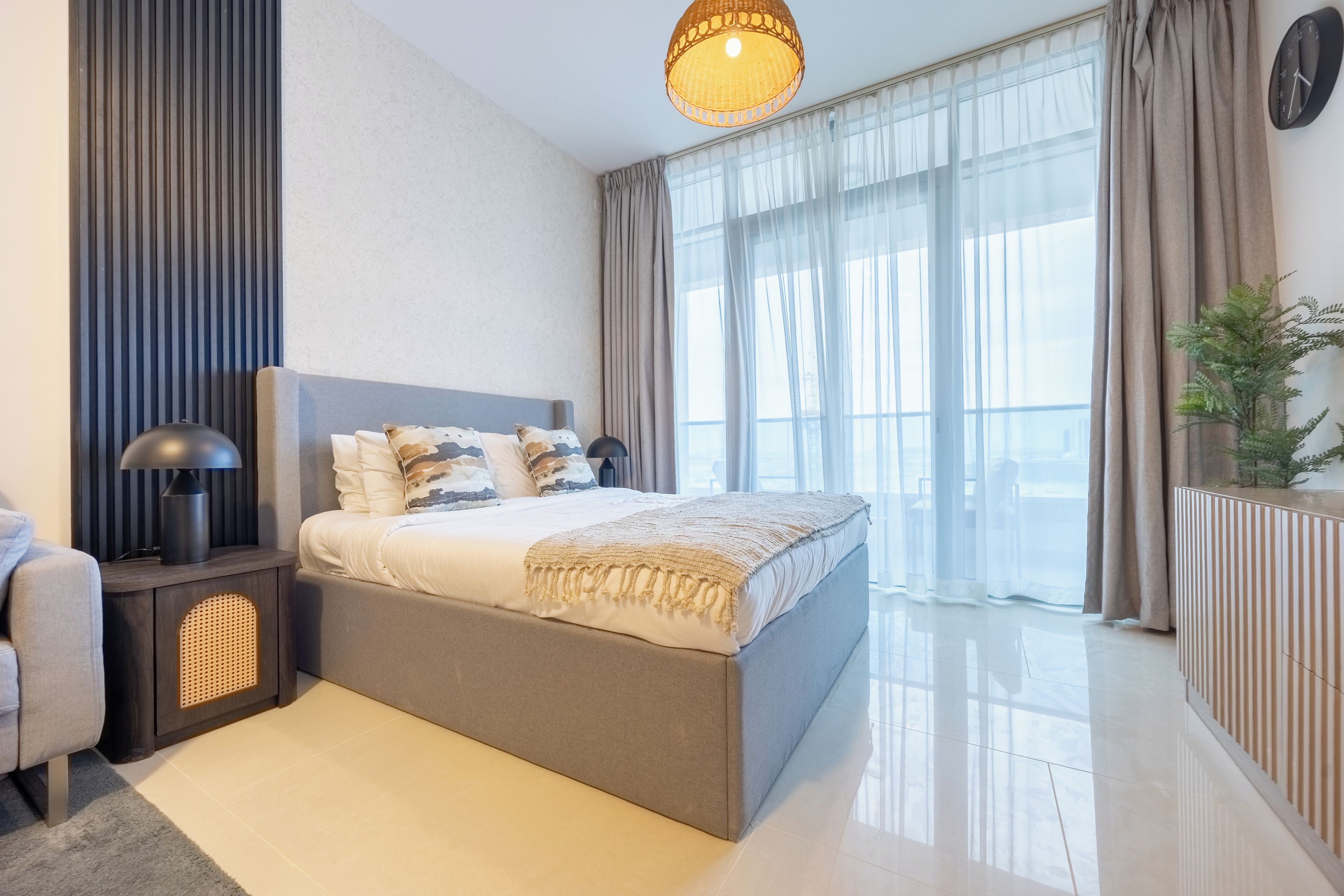 A modern bedroom with a large bed, a bedside lamp, a radiator, and a view of the outdoors through sheer curtains.