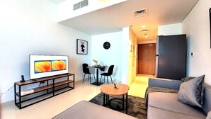 A modern living room with a flat-screen TV, a sofa, a coffee table, and a dining area with chairs. - Bloomfields STU with Canal View Julpur (Abu Dhabi)