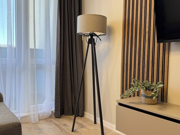 Une chambre moderne avec un lampadaire, un téléviseur fixé sur un mur recouvert de panneaux en bois et une petite table sur laquelle est posée une plante.