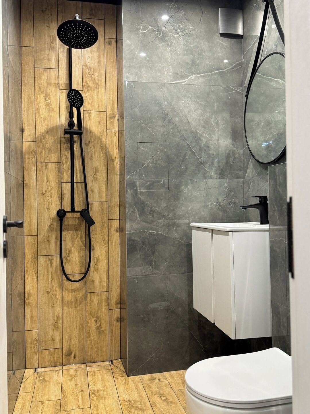 A modern bathroom with a wooden shower enclosure, a white sink, and a mirror.