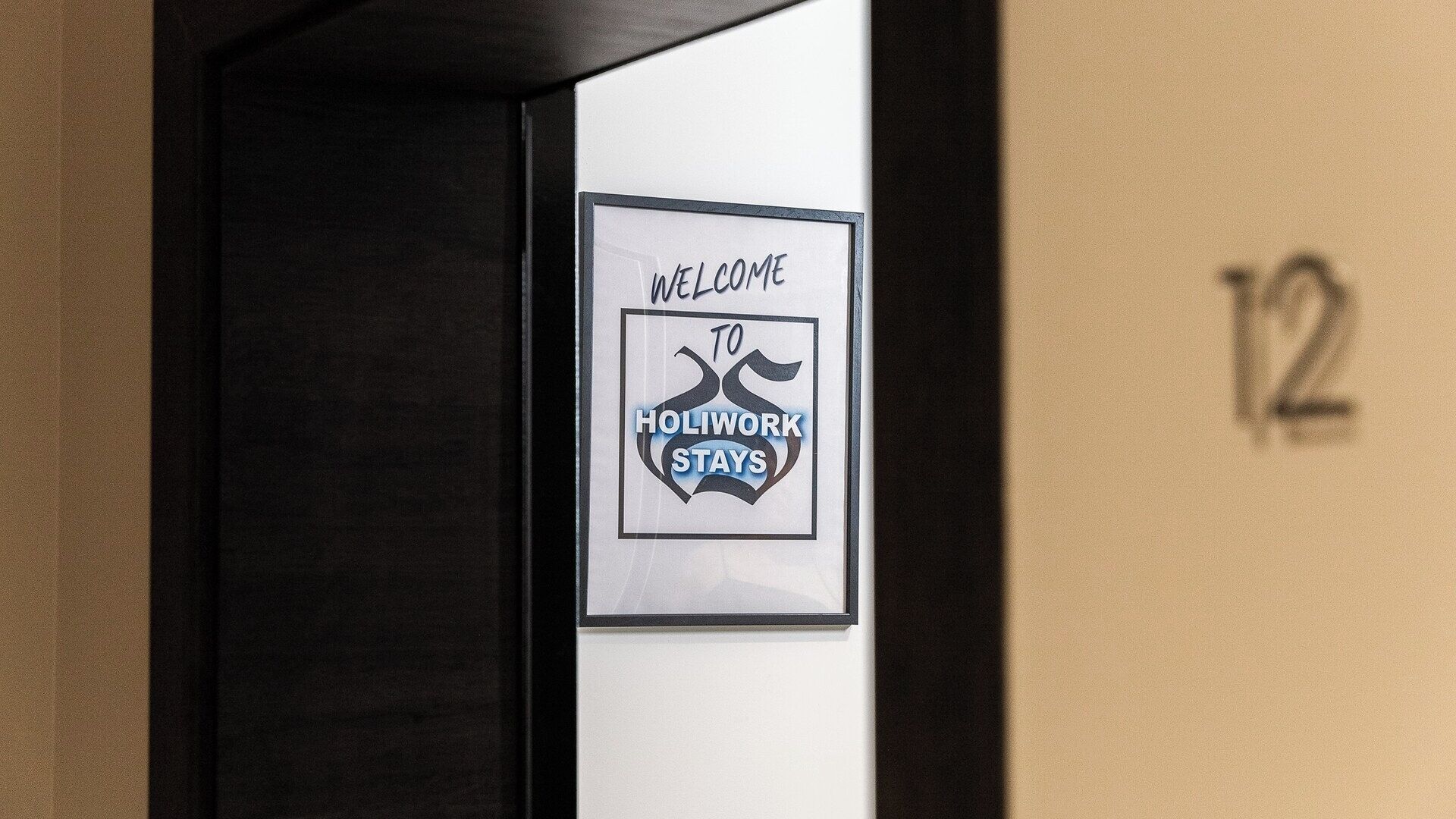 A framed welcome sign for Holiwork Stays with a number '12' on the wall.
