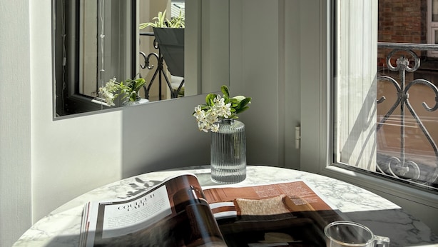 A magazine on a marble table, a glass of coffee, and a vase with flowers by a window. - Home Chic Home – Le Cocon de Paris La Défense (La Garenne-Colombes)