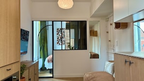 A modern interior with a bed, a wooden cabinet, a hanging light fixture, and a view through a glass door. - Home Chic Home – Le Cocon de Paris La Défense (La Garenne-Colombes)