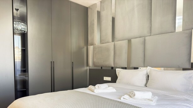A modern hotel room with a large bed, grey wardrobe, and a chandelier. - 2BR Apartment | Free Parking | Central (Plovdiv)