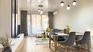 A modern living room with a dining area, featuring a sofa, a coffee table, and a TV. - 2BR Apartment | Free Parking | Central (Plovdiv)