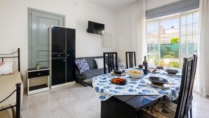 A dining area with a table set for two, a sofa, a TV mounted on the wall, and a view of the outdoors through large windows. - Appartamento Golden Beach Porto Cesareo (Porto Cesareo)