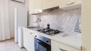 A compact kitchen with a gas stove, sink, and a refrigerator. - Appartamento Golden Beach Porto Cesareo (Porto Cesareo)
