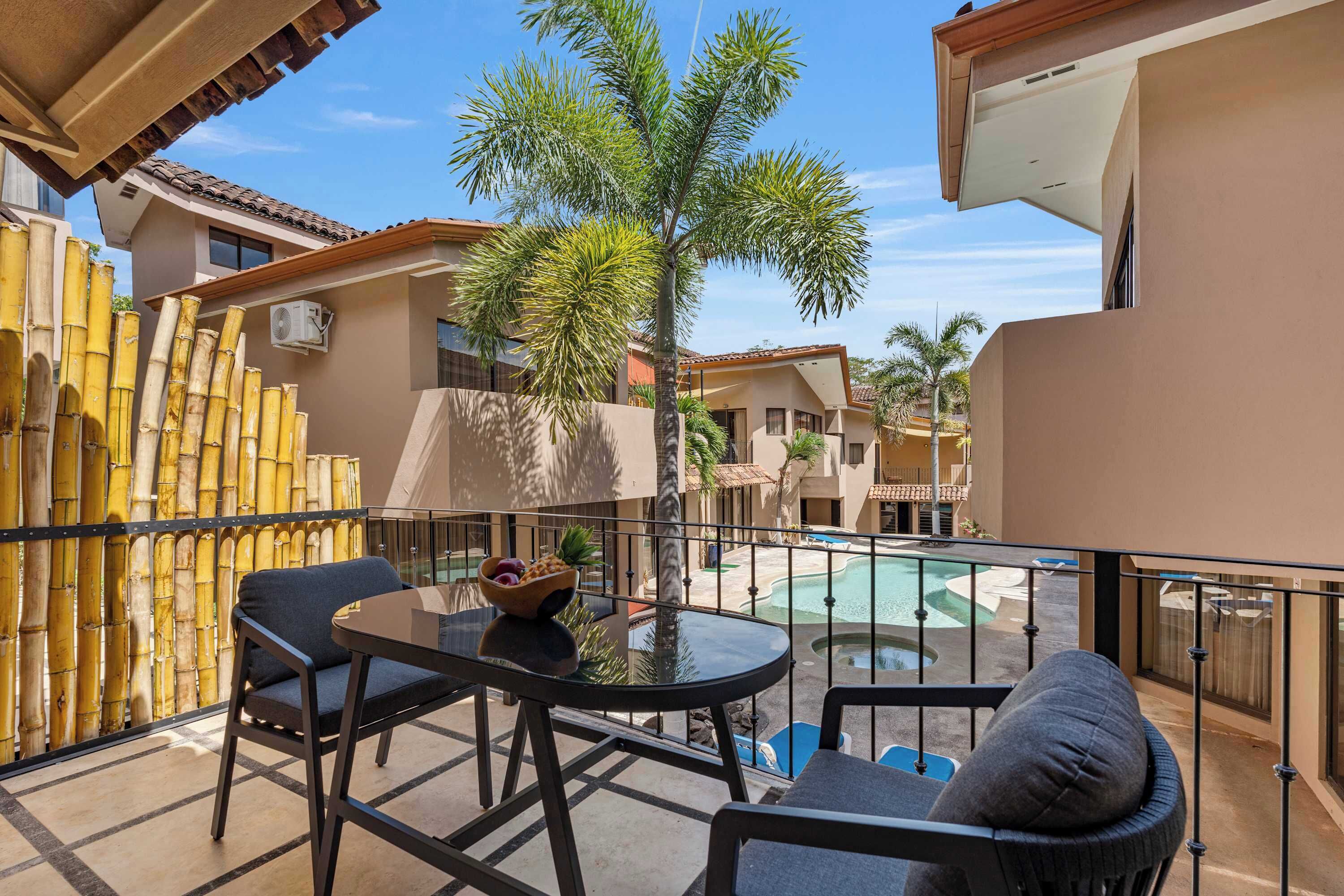 A balcony with a table and chairs, a pool, and a bamboo fence.