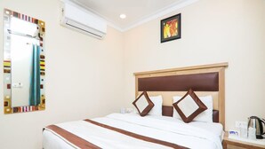 Quarto de hotel com uma cama grande, uma mesa de cabeceira com chaleira, um espelho e um ar condicionado.