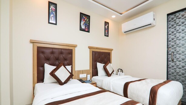 Quarto de hotel com duas camas, cada uma com cabeceira de madeira e roupa de cama branca. Há um ar condicionado fixado na parede e quadros decorativos acima das camas.