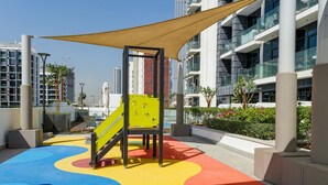 A playground with colorful play area and a yellow slide, surrounded by modern buildings and a clear sky. - Unique Studio in Azizi Riviera (Dubai)