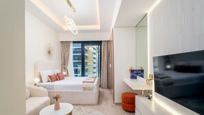 A modern hotel room with a large bed, a TV, a sofa, and a small table. - Unique Studio in Azizi Riviera (Dubai)