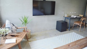 A modern living room with a flat-screen TV mounted on the wall, a wooden dining table with chairs, a small desk with a chair, a potted plant, and a patterned rug. - Tomato TTT Inn (Taipei)