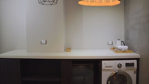 A laundry area with a washing machine, a hanging light fixture, and a small shelf with a kettle and a box. - Tomato TTT Inn (Taipei)