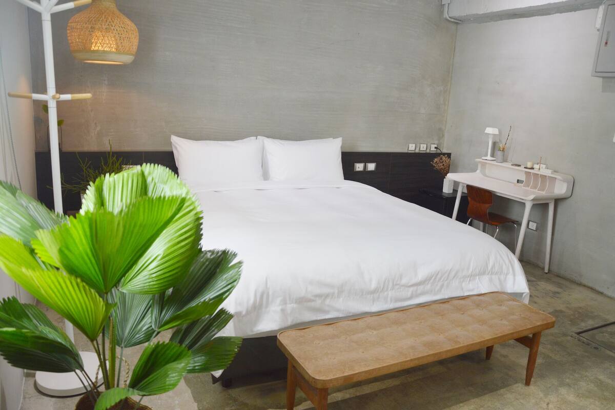 Une chambre moderne avec un lit, une table de chevet, un banc et un luminaire suspendu.