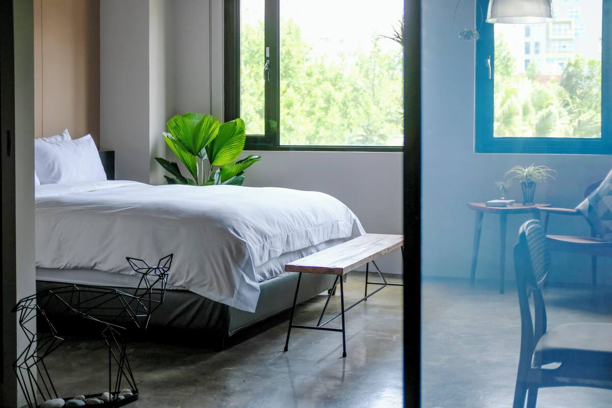 Une chambre à coucher moderne avec un lit, un banc, une plante en pot et une vue sur la verdure à l’extérieur.