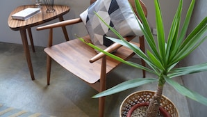 A wooden chair with a geometric-patterned cushion, a small table with a plant, and a potted plant with long leaves. - Tomato TTT Inn (Taipei)