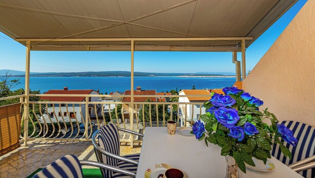 A balcony with a view of the sea, a table with chairs, and a vase of blue flowers. - Apartman Franjo 2 (Dramalj)