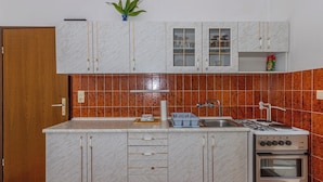 A compact kitchen with a built-in stove, oven, and sink, featuring white cabinets and a tiled backsplash. - Apartman Franjo 2 (Dramalj)
