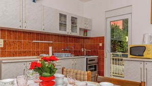 A kitchen with a dining area, featuring a stove, oven, microwave, and a window with a view of greenery. - Apartman Franjo 2 (Dramalj)