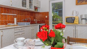 A kitchen with a tiled backsplash, a microwave, a coffee maker, and a dining table set with a vase of red flowers. - Apartman Franjo 2 (Dramalj)