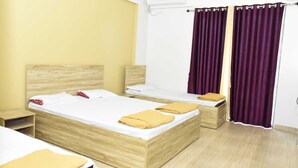 A room with two beds, wooden headboards, a small bedside table, a nightstand, a wall-mounted air conditioner, and purple curtains. - Hotel Amit Palace (Ambegaon)