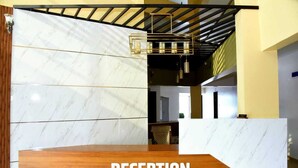 A reception area with a marble wall, a wooden reception desk, and a hanging light fixture. - Hotel Amit Palace (Ambegaon)