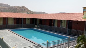 A hotel with a swimming pool, brick buildings, and a mountainous backdrop. - Hotel Amit Palace (Ambegaon)